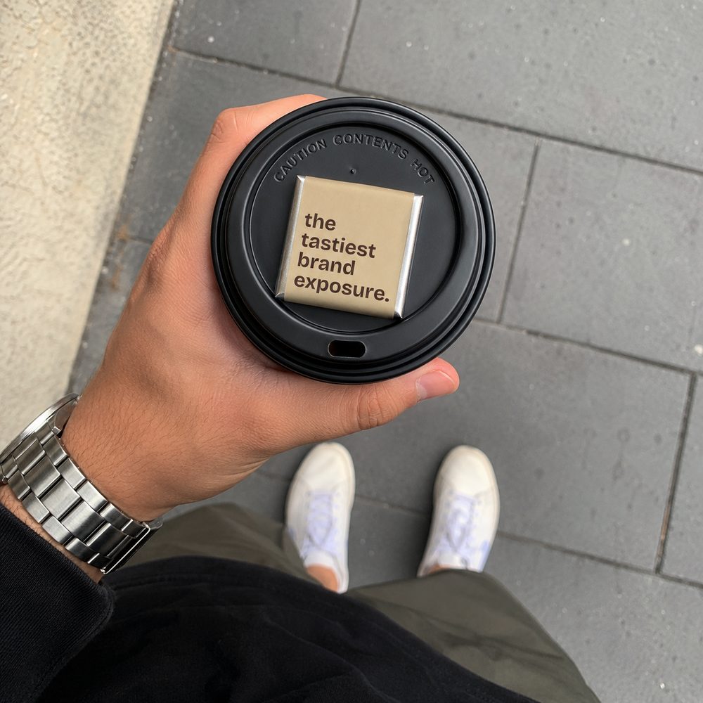 a kakao chocolate square resting on a takeaway coffee lid, held in hand on a sydney street